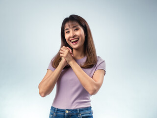 Fototapeta premium Asian woman with long straight hair wearing purple t-shirt and jeans smiling warmly with hands clasped in front of chest, showing cheerful and kind expression in light studio background
