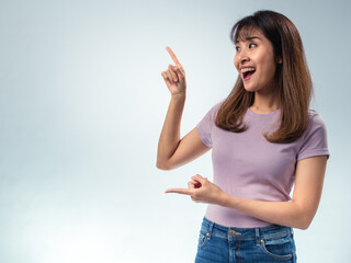 Asian woman in purple t-shirt and jeans smiling brightly while pointing upward with one finger,...