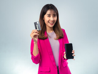 Asian woman in pink blazer and purple t-shirt smiling while holding a smartphone in one hand and a...