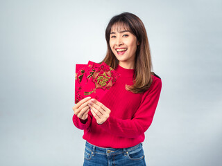 Smiling Asian woman in red sweater holding three red Chinese New Year envelopes, posing cheerfully...