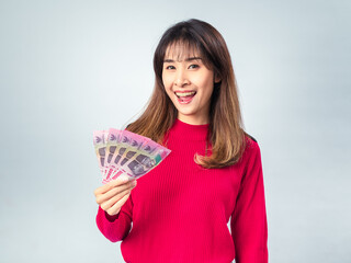 Asian woman in red sweater smiling while holding a fan of Indonesian 100,000 Rupiah banknotes in...