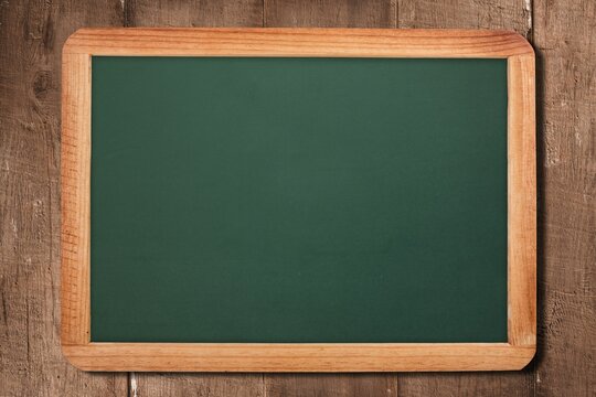 Fototapeta Framed green chalkboard resting against rustic plank backdrop in flat design, showing blank surface