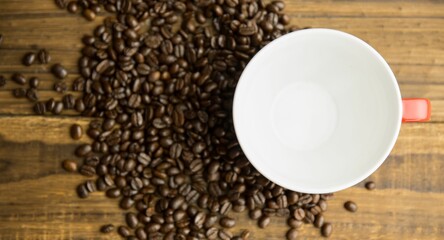 Flat design is showing dark roasted beans and red-handled white coffee cup resting on wood tabletop