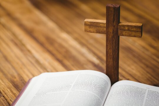 Wooden cross by bible on hardwood flooring
