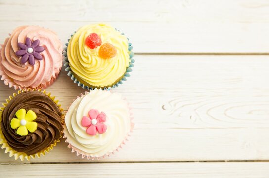 Naklejki Showing four cupcakes on tabletop, showcasing pastel frosting, fondant flowers, gummies