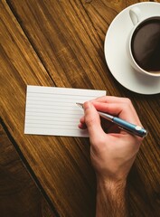 Cropped hand writing on paper at desk with coffee cup
