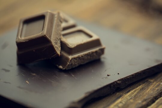 Naklejki Two dark chocolate squares are resting on slate board over rustic wooden tabletop in flat design