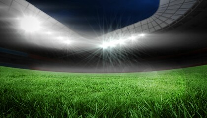 Empty stadium grass field is shining under curved roof canopy, floodlights flaring against navy sky