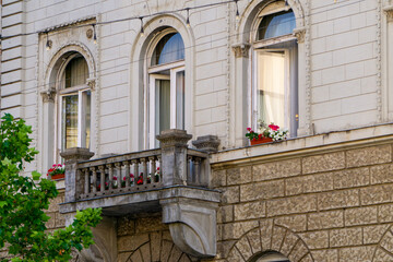 Facade of a historic tenement house with a decorative stone balcony and three tall arched windows....