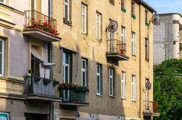 Facade of an old tenement house with balconies, flower boxes, and satellite dishes, photographed on a sunny day in Ł&oacute;dź