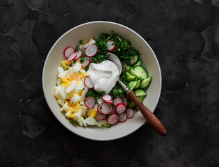 Eggs, cucumbers, radishes, green onions and Greek yogurt salad on a dark background, top view