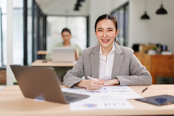 Obraz premium Asian professional analyst business woman sitting at office desk working on laptop thinking on project plan, analyzing marketing or financial data online, watching elearning webinar. 