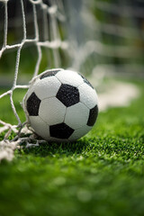 Fototapeta premium A soccer ball resting in the net on a green field in a close up shot showing the details of the ball