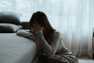 Obraz premium A young woman sits alone on a couch, holding her head in distress. The mood is somber, suggesting stress, anxiety, or emotional exhaustion at home.