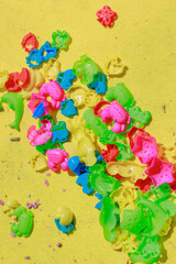 Scattered colorful play shapes mixed with kinetic sand on a yellow carpet.