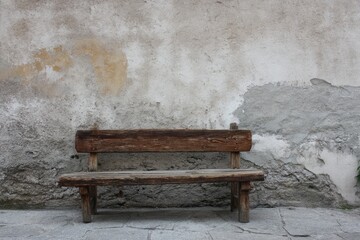 Weathered wooden bench sits before a crumbling, textured wall, showing age and quiet solitude