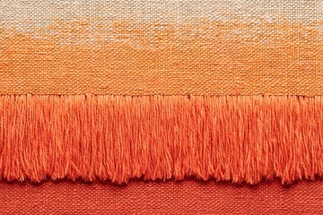 Fototapeta premium Close-up view of a vibrant orange and beige textile with a prominent fringe. The gradient color transition and textured weave create a visually appealing detail.