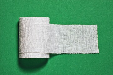 A roll of white, loosely woven fabric bandage partially unrolled against a green background