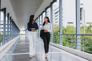 Fototapeta premium Two businesswomen walking and talking on skywalk bridge