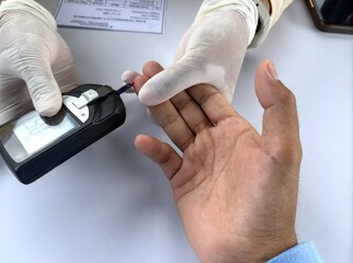 Healthcare worker applies a blood drop to a glucose test strip using a glucometer during a routine blood sugar screening.