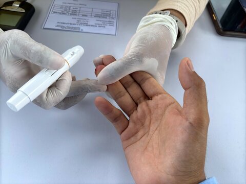 A nurse uses a lancet device to prick a patient's finger for a blood sugar test during a public health screening.