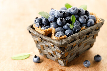 Ripe blueberries in wicker basket on wooden table.