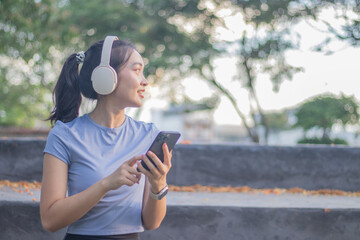 Naklejka premium A smiling young Asian woman jogs outdoors under the spring sunshine, enjoying exercise, independence and well-being. Her energetic movements reflect inspiration, strength and a healthy lifestyle.