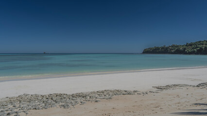 A beautiful beach on a tropical island, without people. Calm turquoise ocean, white sand, clear blue sky. A green hill in the distance. Copy space. Madagascar. Nosy Iranja