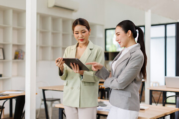Two asian business finance market analyst in standing working at office .Business women analyze document Graphs and diagramm on tablet laptop screen.
