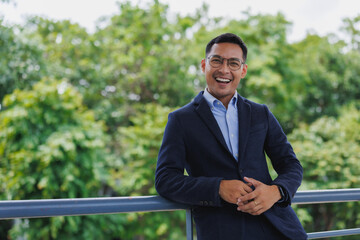 Smiling businessman leaning on railing in green urban environment
