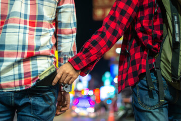 A thief secretly steals a wallet filled with cash from a man's back pocket on a crowded city street at night, highlighting urban crime and public safety issues.