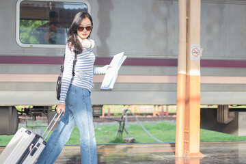 A cool young woman walks alone through a city train station, dragging her suitcase with...