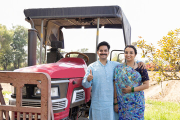 Happy Indian couple with tractor on agriculture field