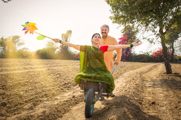 Wife and husband having fun on pushcart over agricultural field.