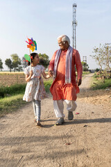 Fototapeta premium Happy grandfather with cute little girl running carefree and having fun with colorful pin wheel at green field.