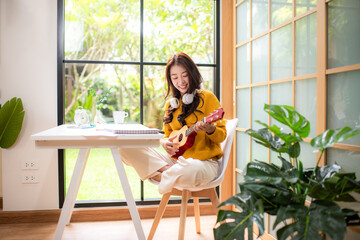 Young woman happy listen music for chill and playing guitar after finish work.   Lifestyle girl using laptop for meeting and working  in living room at home.  Lifestyle Concept