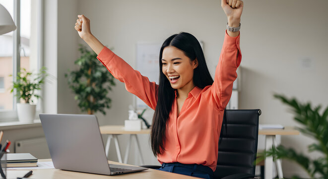 Happy businesswoman celebrating success at her desk using laptop computer in modern office