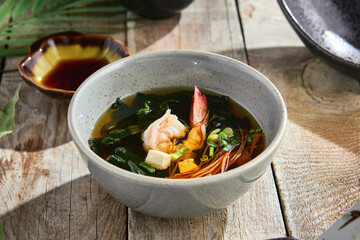 Miso soup with shrimp in natural sunlight, rustic wooden tabletop, overhead composition