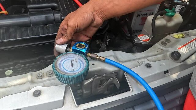 Auto mechanic checking car AC refrigerant pressure with gauge to detect leakage. Vehicle air conditioning maintenance and freon level inspection in a garage.