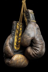 A pair of vintage brown leather boxing gloves, laced and worn, hang against a stark black background.  The gloves show significant age and use
