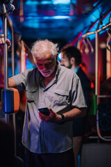Senior man using smartphone on night bus ride