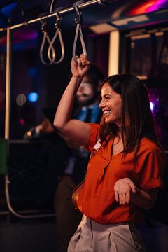 Fototapeta Happy young woman holding handrail on night bus ride home