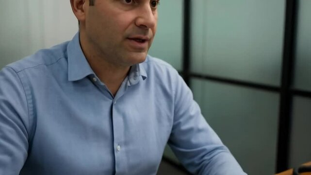 A businessman sits at his desk in an office, actively engaged in a conversation, his hands gesturing emphatically