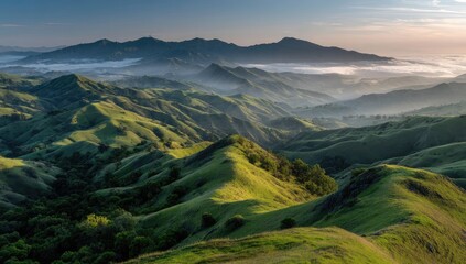 Panoramic view of sunlit, rolling green hills and distant mountains shrouded in morning mist