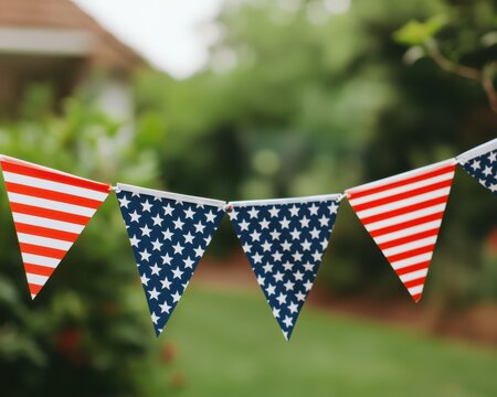 Triangular American flag pennant banners hang outdoors with greenery and a house blurred in the background.