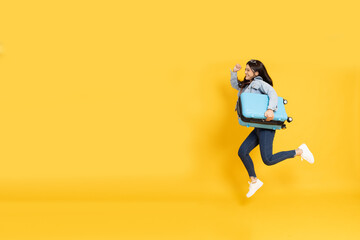 Happy Young Asian traveler woman jumping with blue suitcase bag isolated on yellow background,...