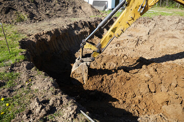 Fototapeta premium A digger operates in a rural setting, carefully excavating a deep trench.