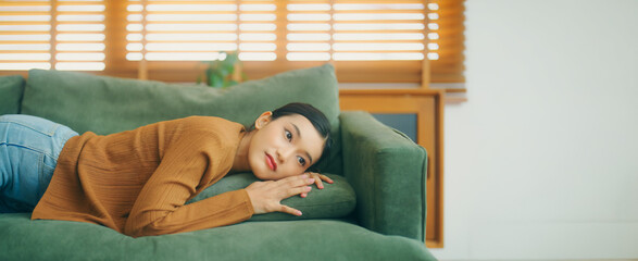 Asian woman resting at home on couch, feeling exhausted after work, lacking energy, or overworked, too tired, and lacking motivation