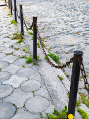 A row of metal poles with chains on a cobblestone sidewalk