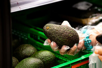 A person carefully selects a ripe avocado from a crate, emphasizing the importance of choosing...